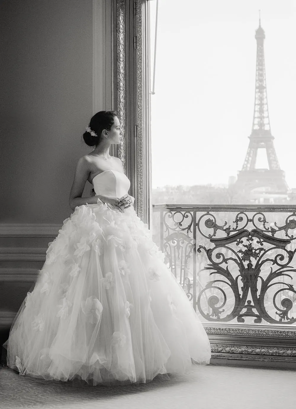 Mariée en robe volumineuse près d’une fenêtre avec vue sur la tour Eiffel