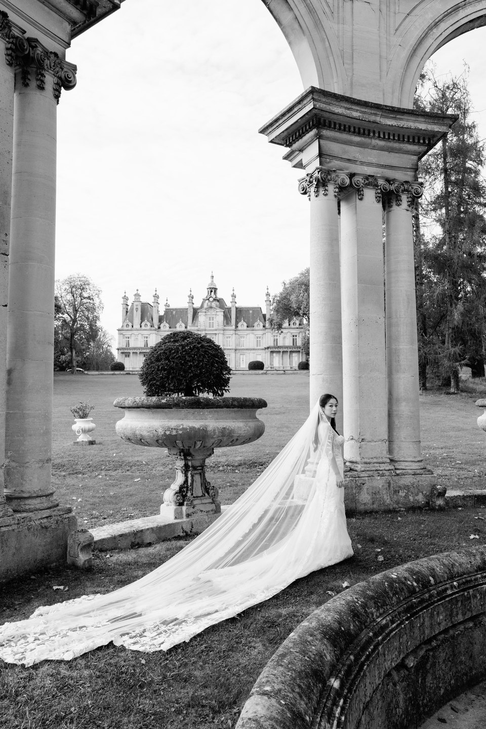 Portrait de mariée en noir et blanc sous les arcades, avec un long voile, par Jérémy Froeliger, photographe de mariage à Paris