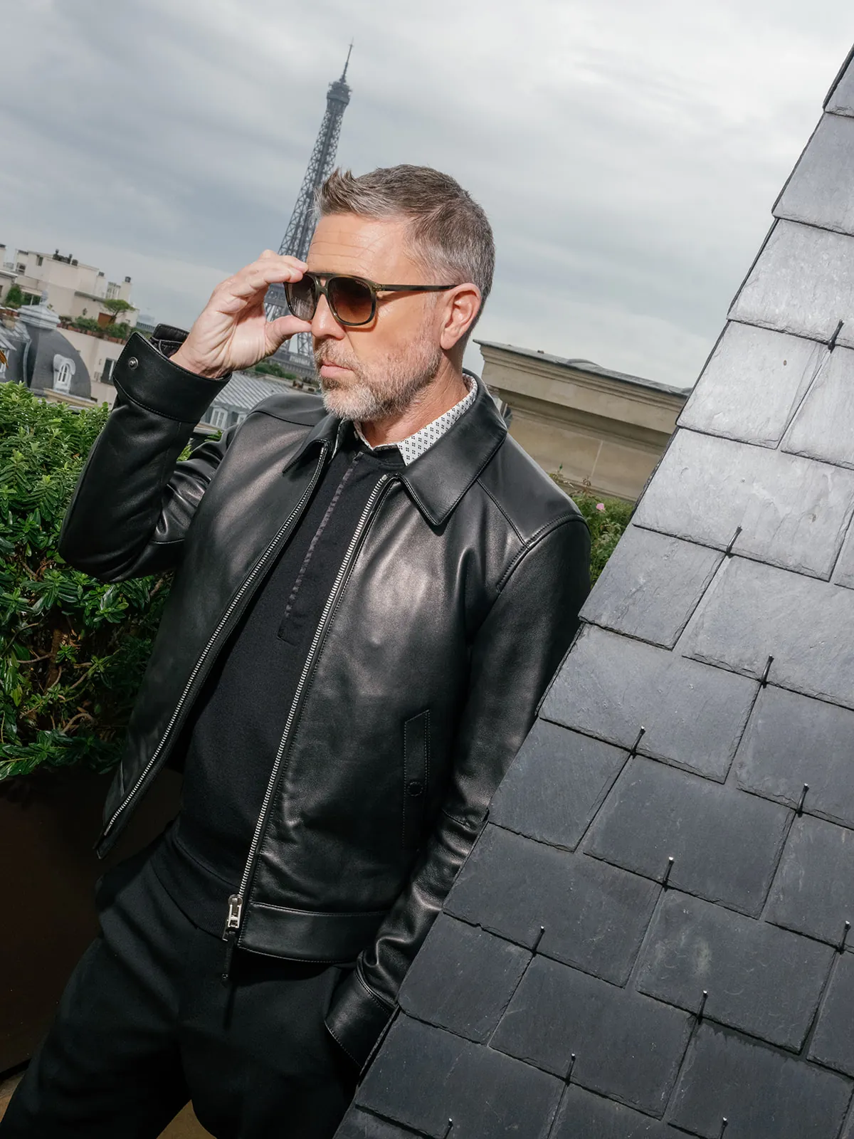 Homme ajustant ses lunettes sur un rooftop parisien, en blouson de cuir noir