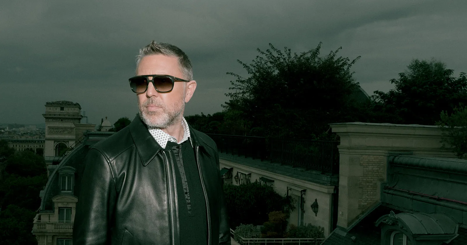 Homme en blouson de cuir noir sur les toits de Paris, avec l’Arc de Triomphe en arrière-plan