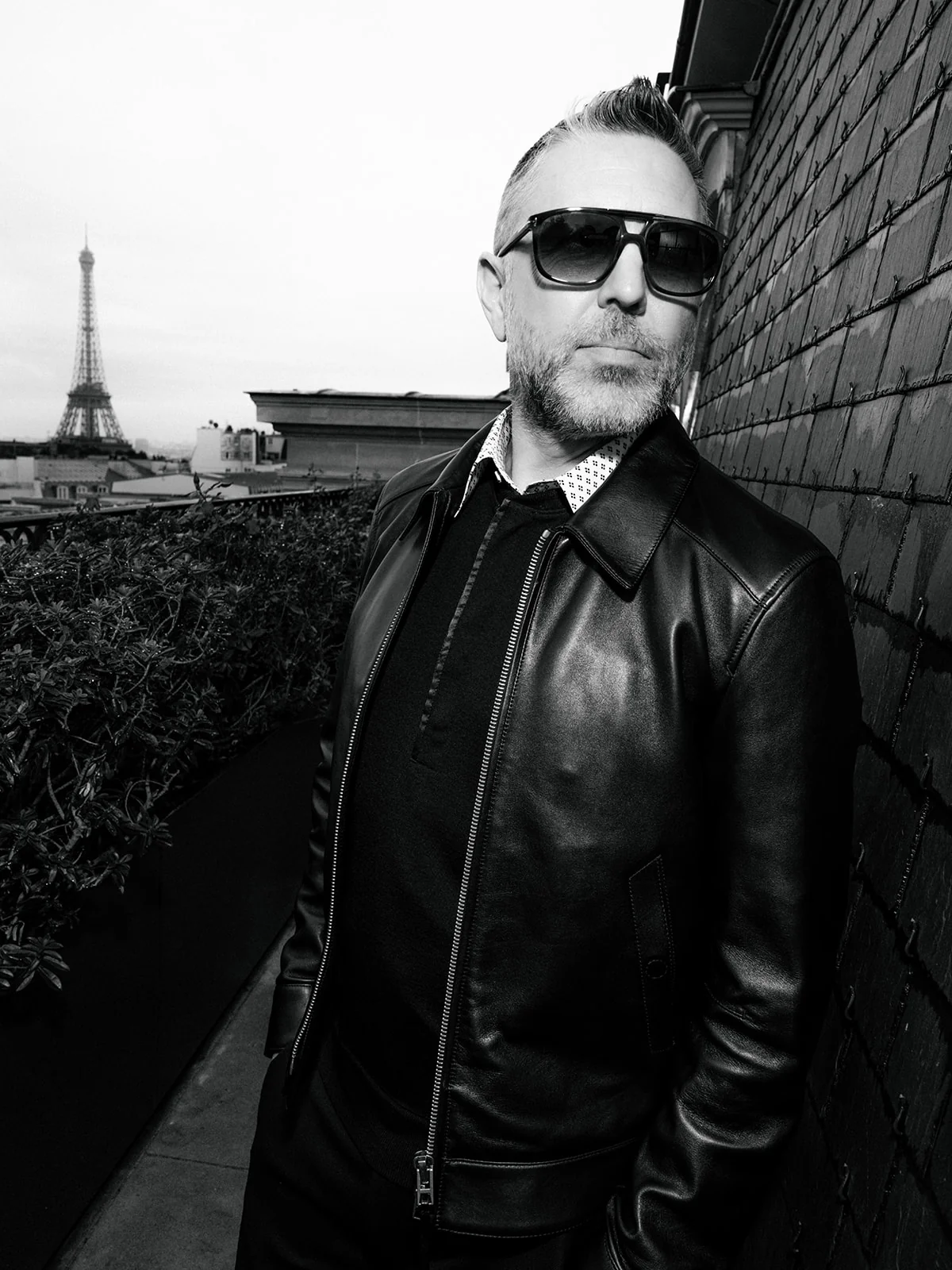 Portrait en noir et blanc d’un homme en blouson de cuir et lunettes, devant la tour Eiffel
