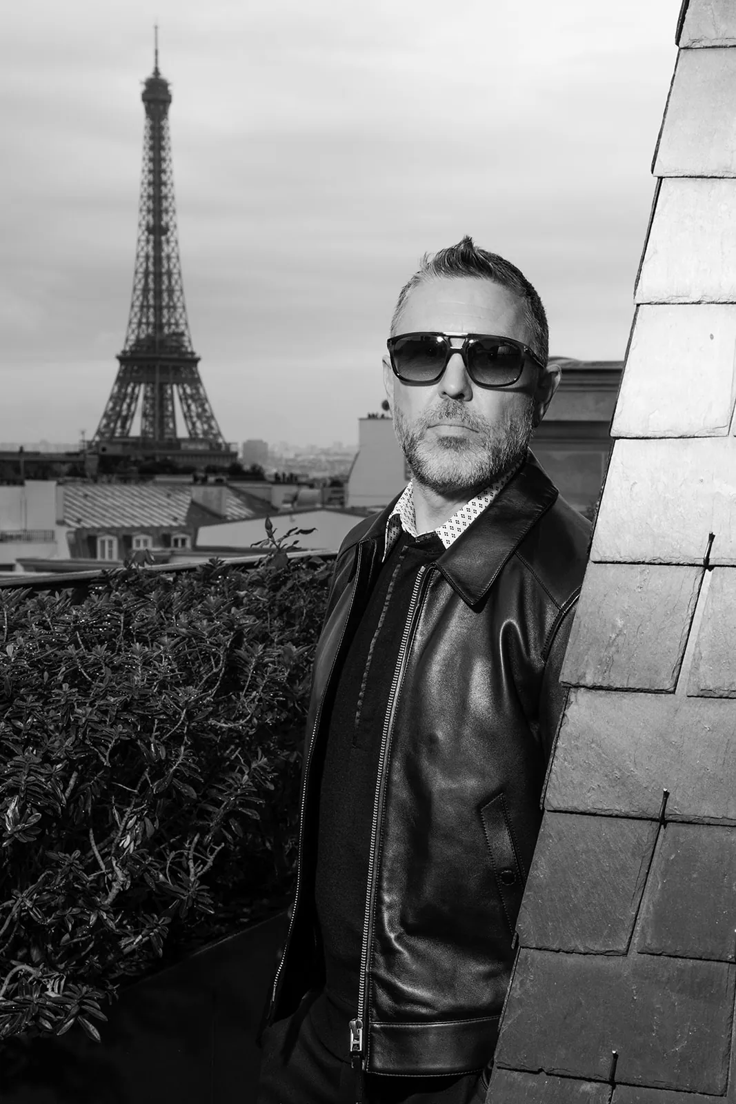 Portrait en noir et blanc d’un homme en cuir noir avec la tour Eiffel en arrière-plan