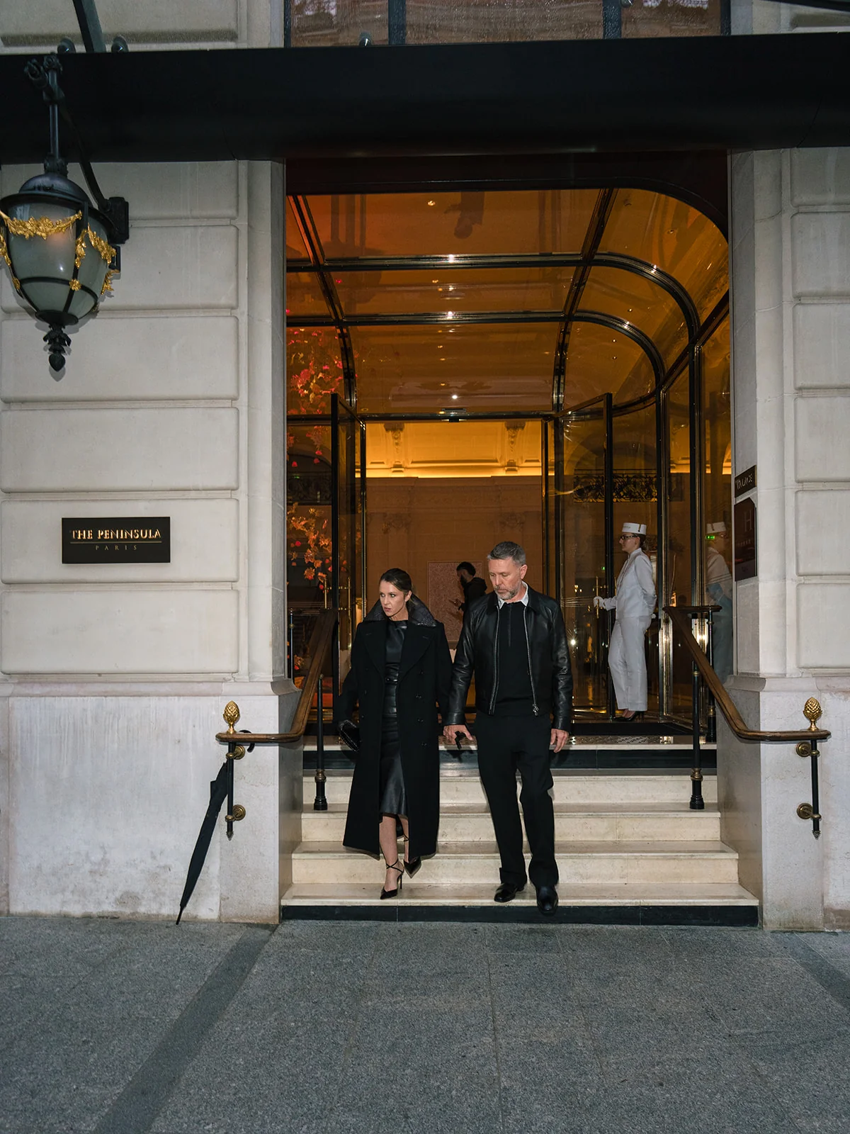 Couple in black outfits descending the steps at the entrance to The Peninsula Paris