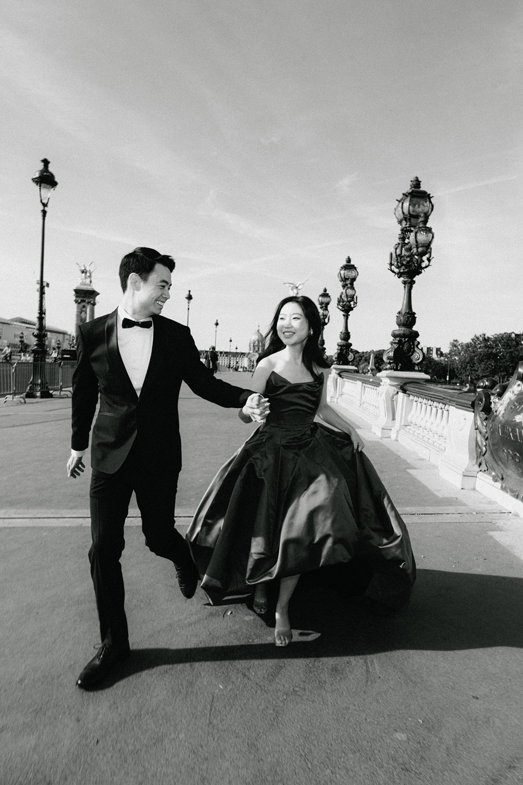 Black and white editorial pre-wedding couple walking across Pont Alexandre III in Paris