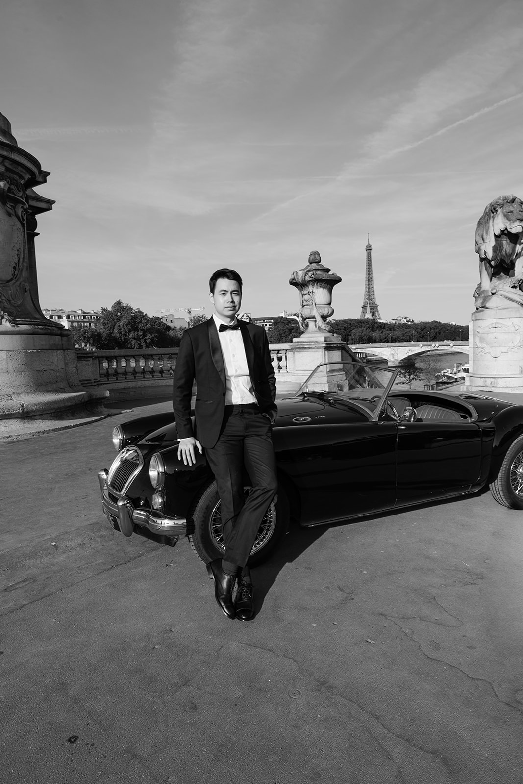 Black and white editorial groom portrait with a vintage MG roadster and Eiffel Tower in Paris