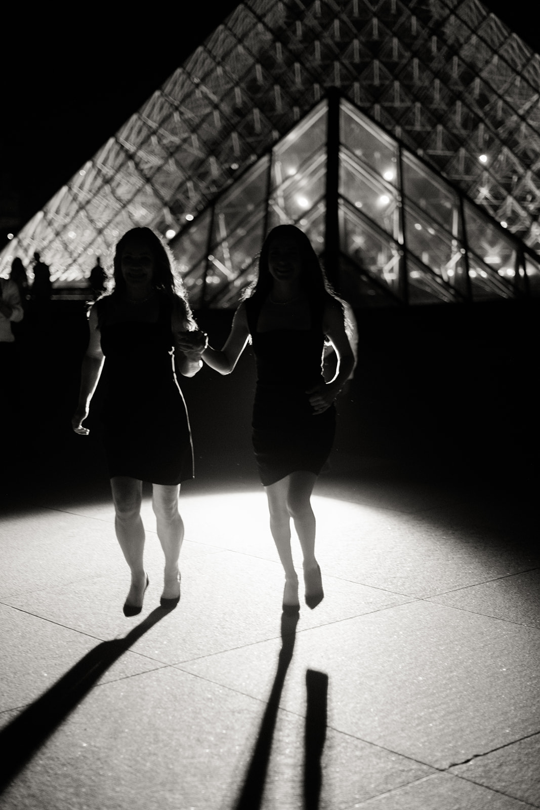 Couple walking in silhouette beside the Louvre Pyramid at night