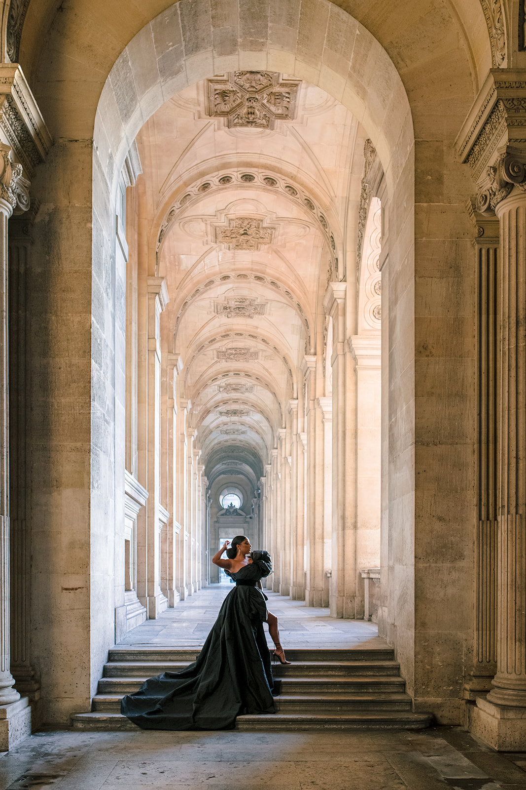Candice Craig posing in a dramatic black gown beneath the Louvre arcades in Paris