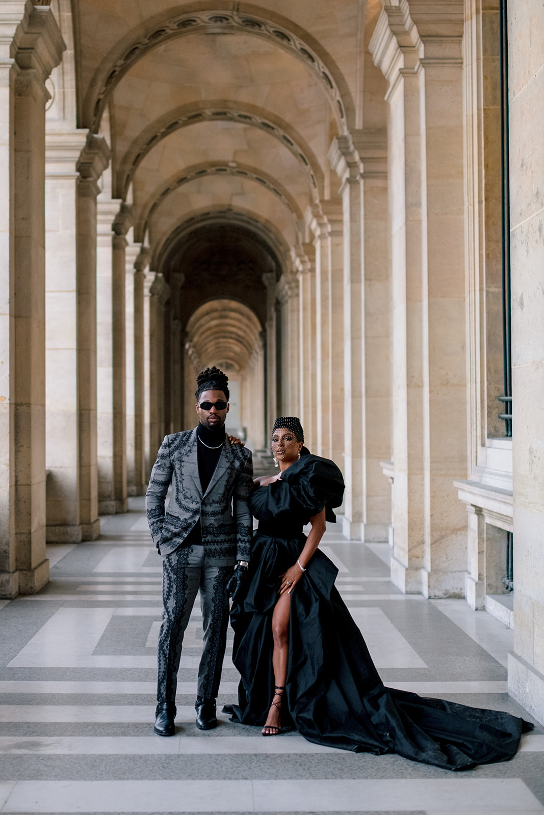 Candice Craig and Omar Bolden framed by the long Louvre arcades in Paris