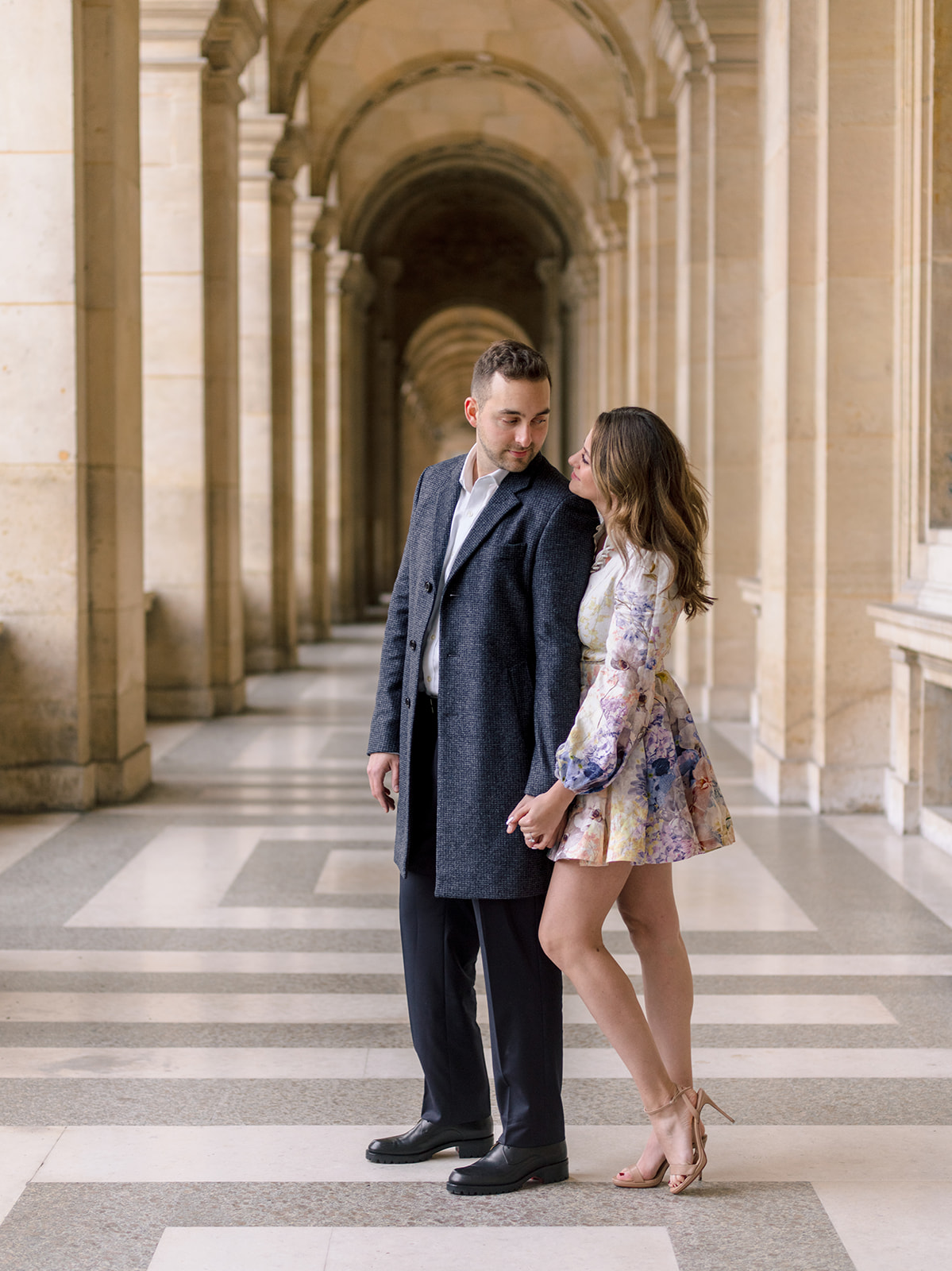 American couple walking beneath the Louvre colonnade during their Paris photoshoot