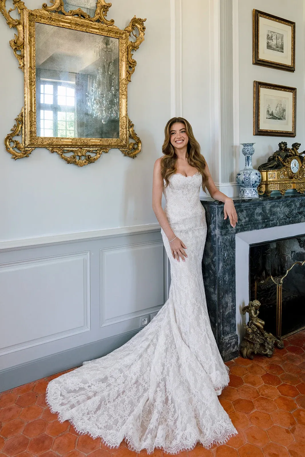 Bride in a lace wedding dress beside a marble fireplace at Villa Baulieu