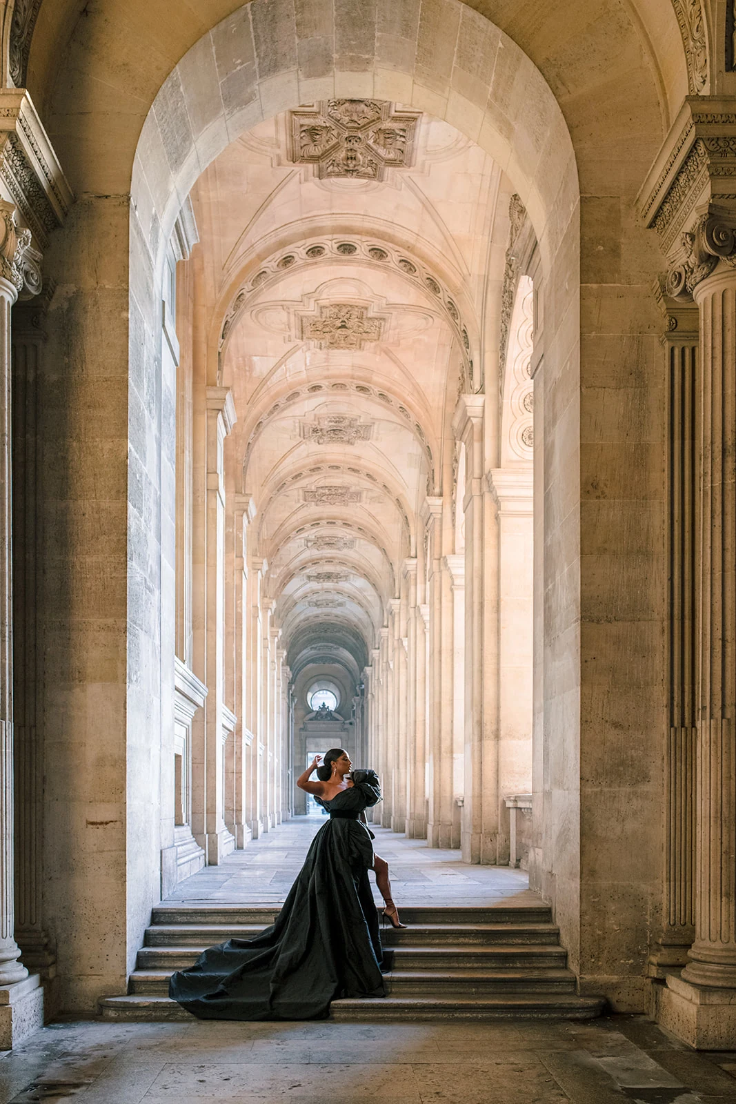 Candice Craig posing in a dramatic black gown beneath the Louvre arcades in Paris