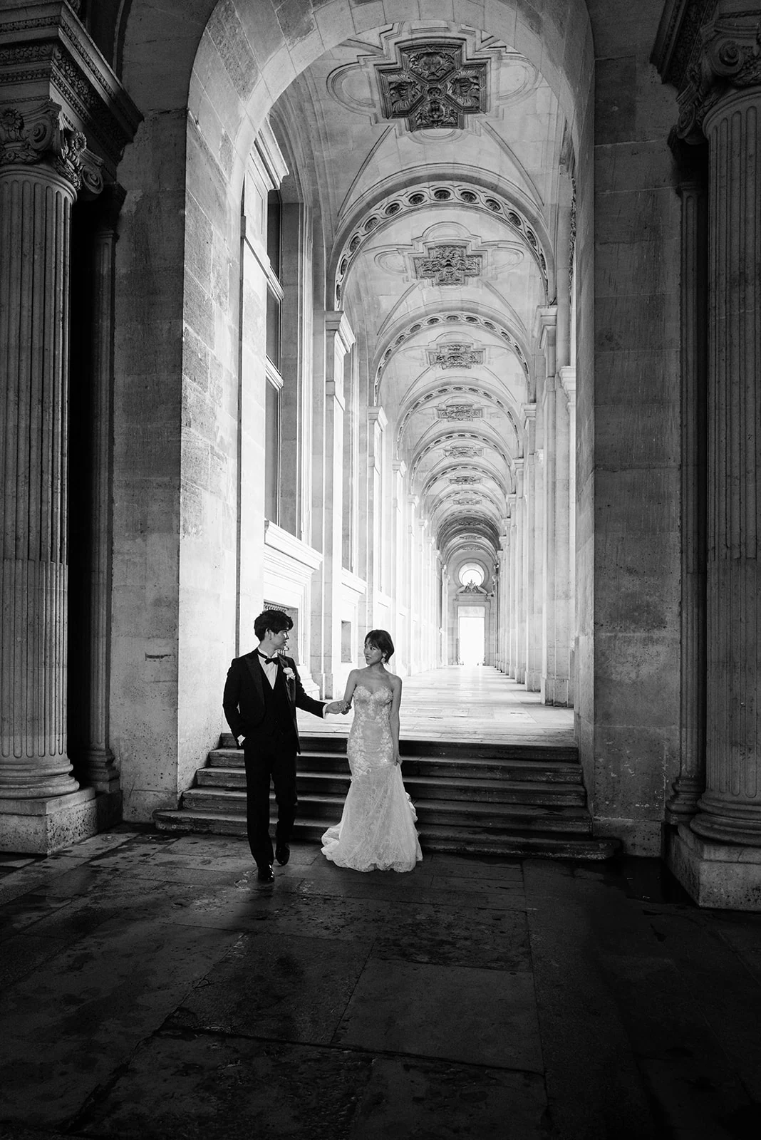 Couple walking beneath the Louvre colonnade during an elegant Paris photoshoot