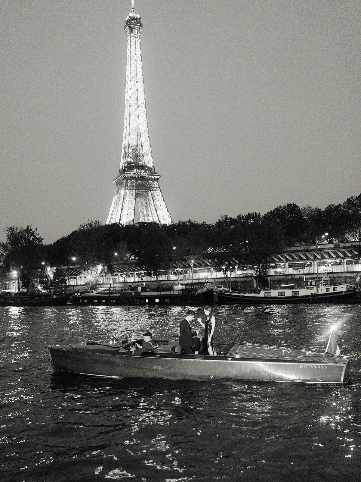 Black and white view of an engaged couple on a boat beneath the Eiffel Tower