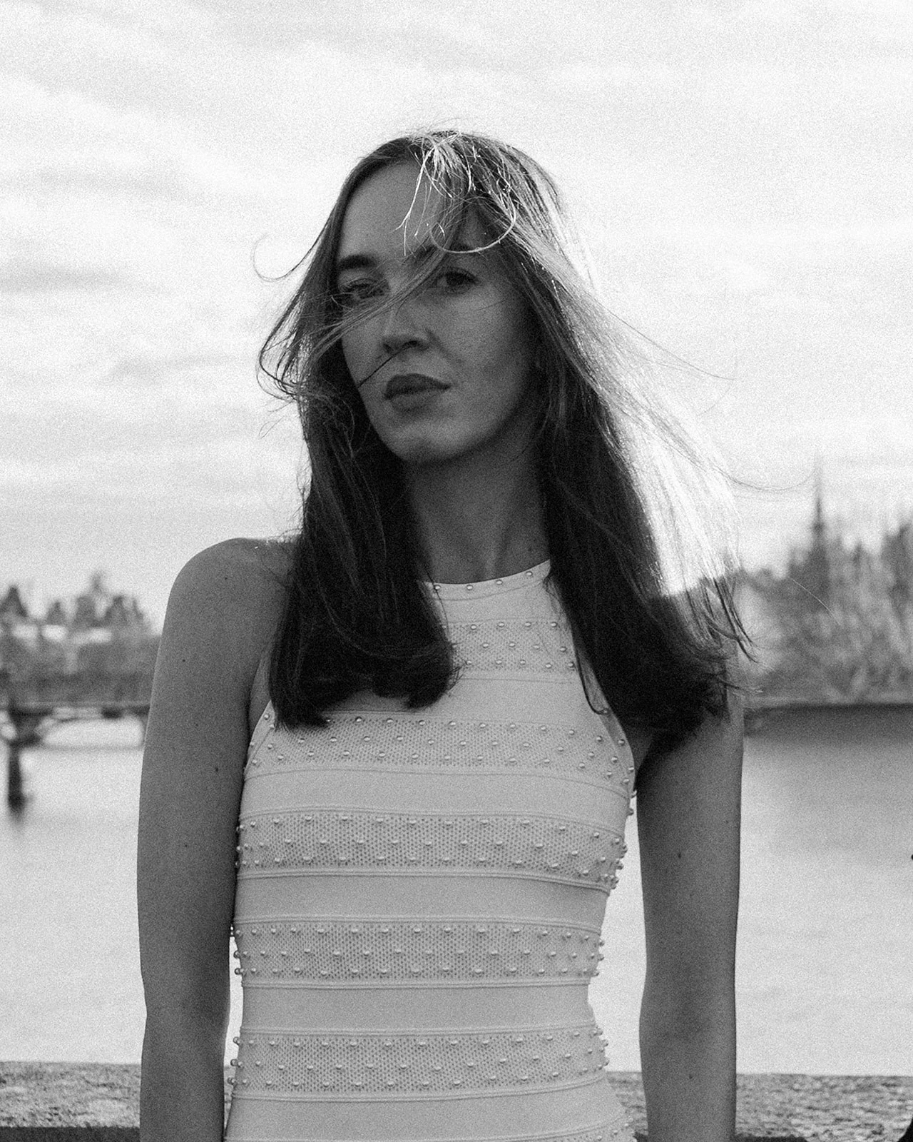 Black-and-white editorial portrait of a woman in a white beaded dress beside the Seine in Paris