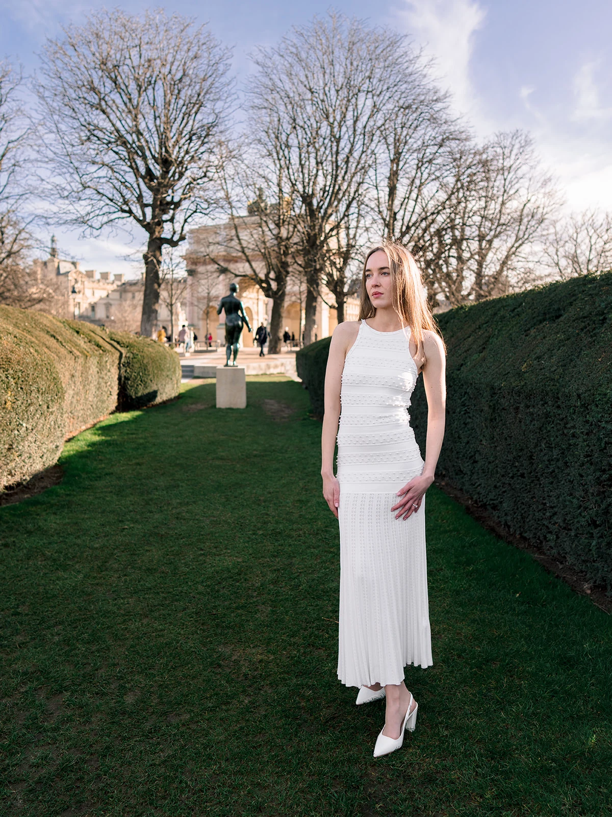 Editorial portrait in a white dress between the sculpted hedges of the Tuileries Garden