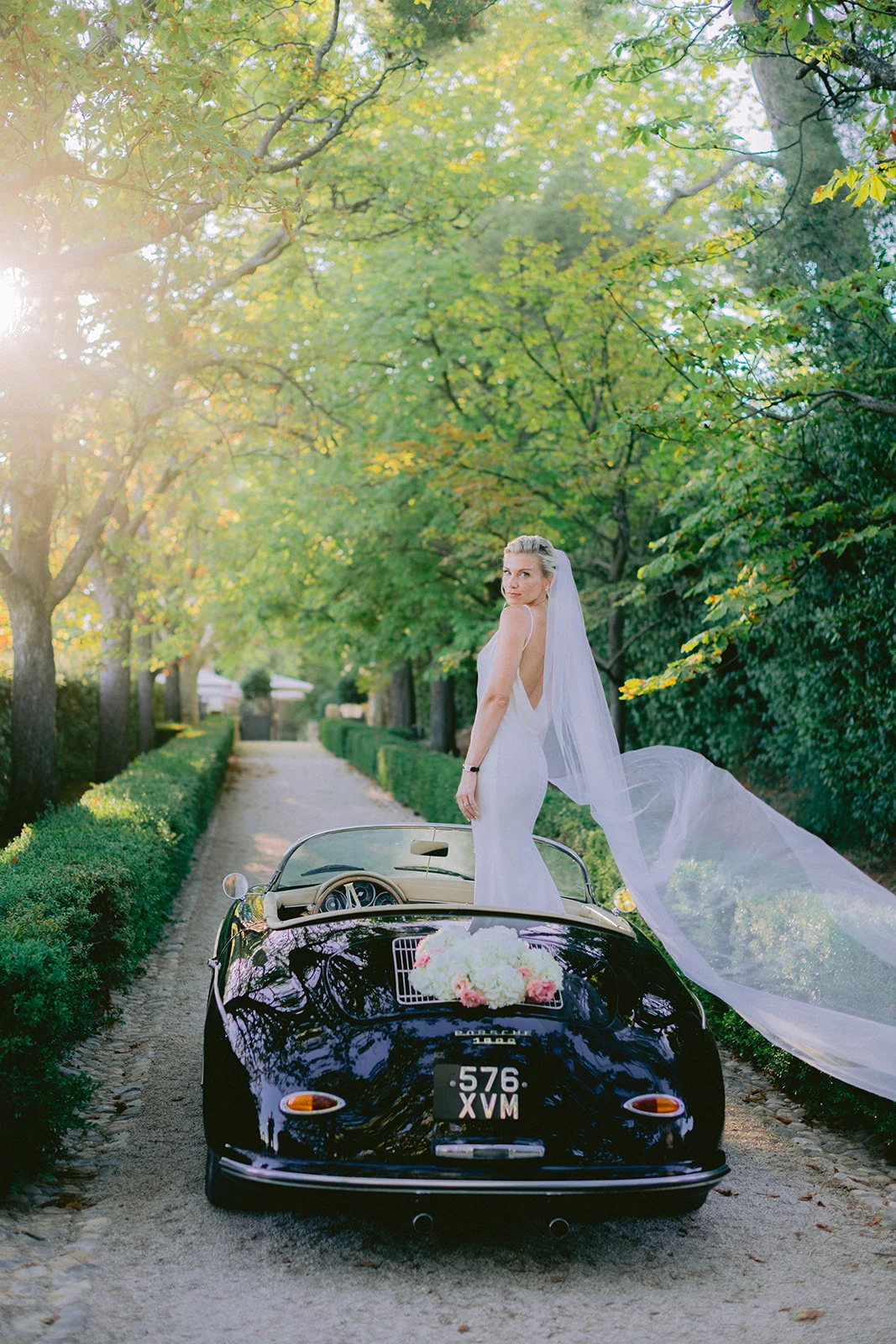 Bride posing on a Provence classic car with her veil